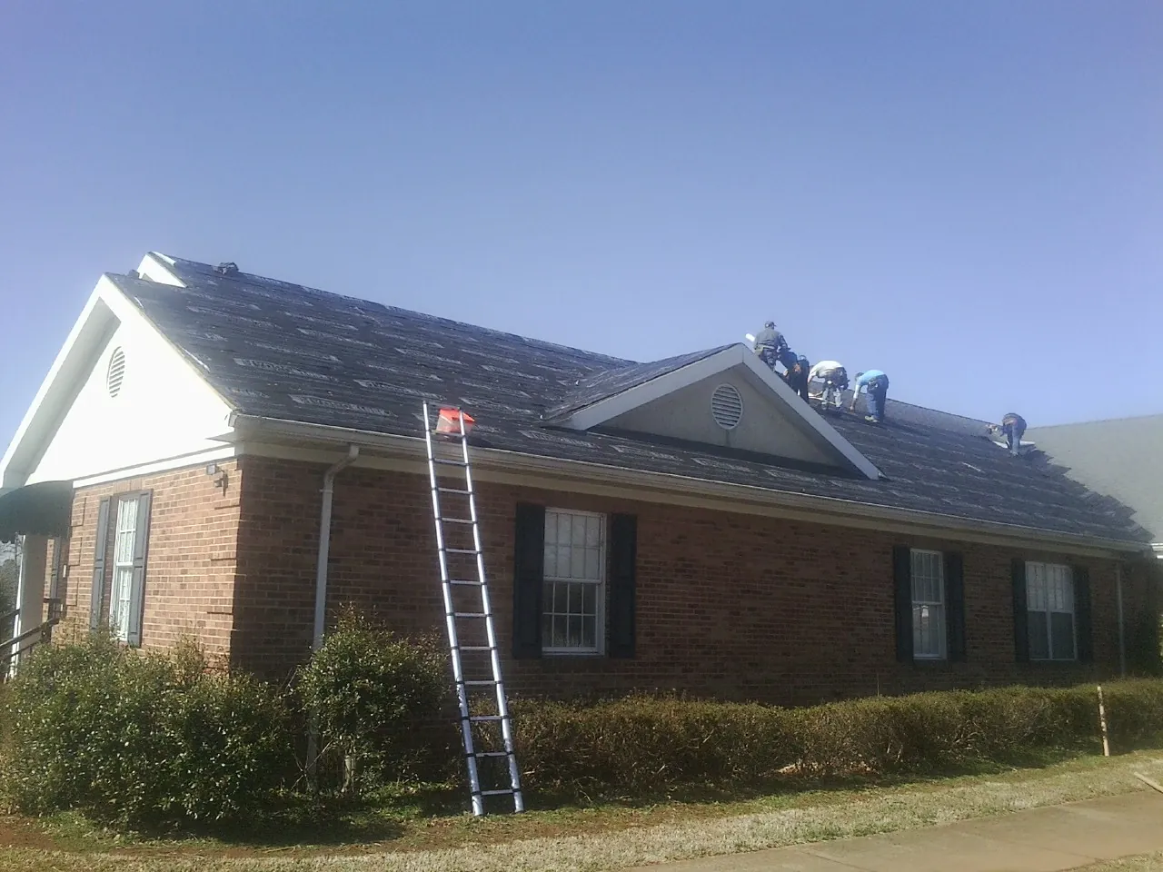 Crew tearing shingles off a brick ranch roof with a ladder set — Emergency Roof Repair work by our crew in Los Angeles