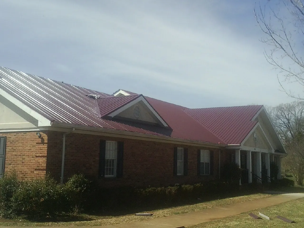 Red metal roof with gabled entries on a long brick building, from a Hail Damage Roof Repair job in Los Angeles