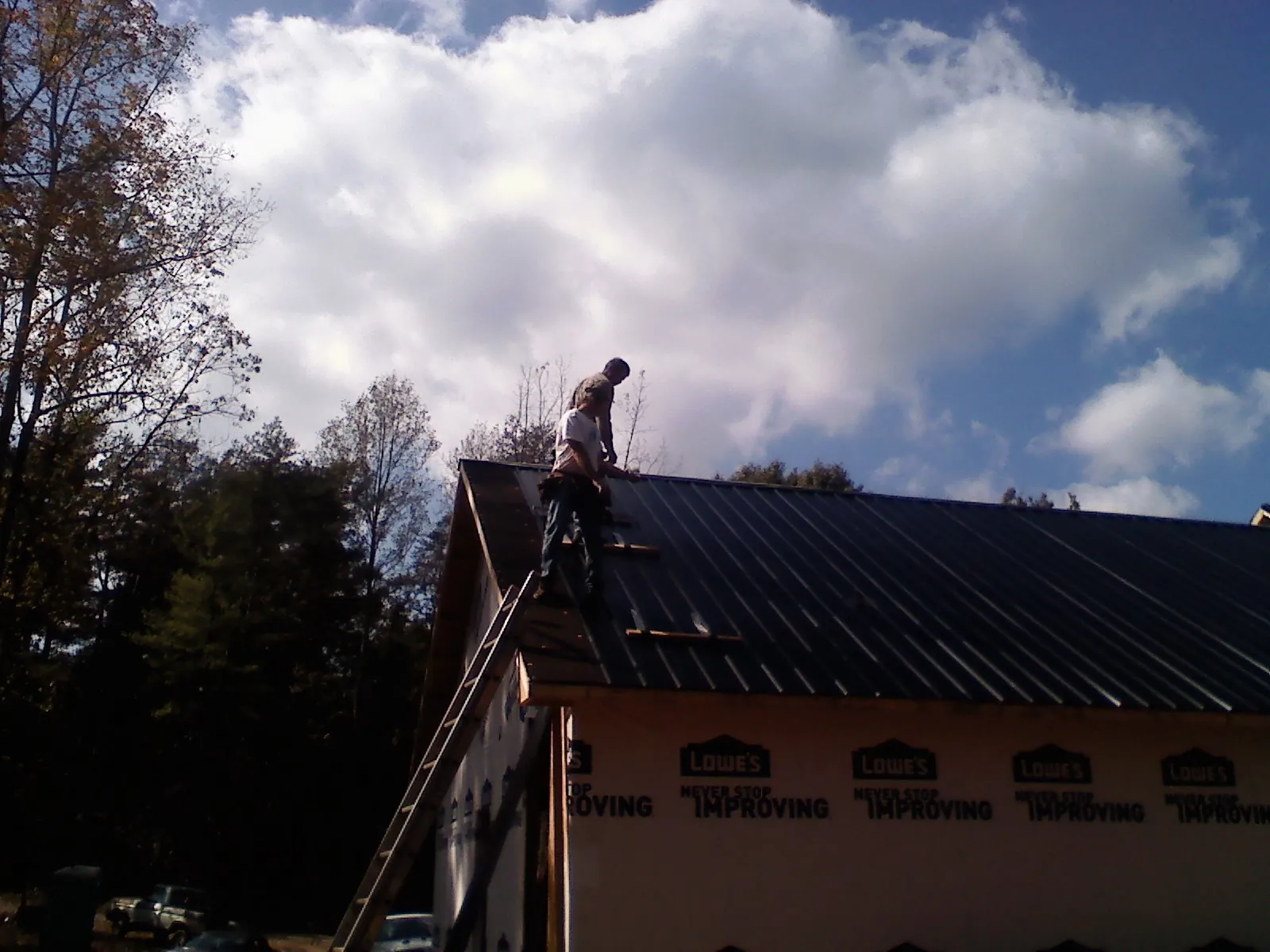 Roofer fastening dark metal panels high against a cloudy sky, from a Roof Inspection job in Los Angeles