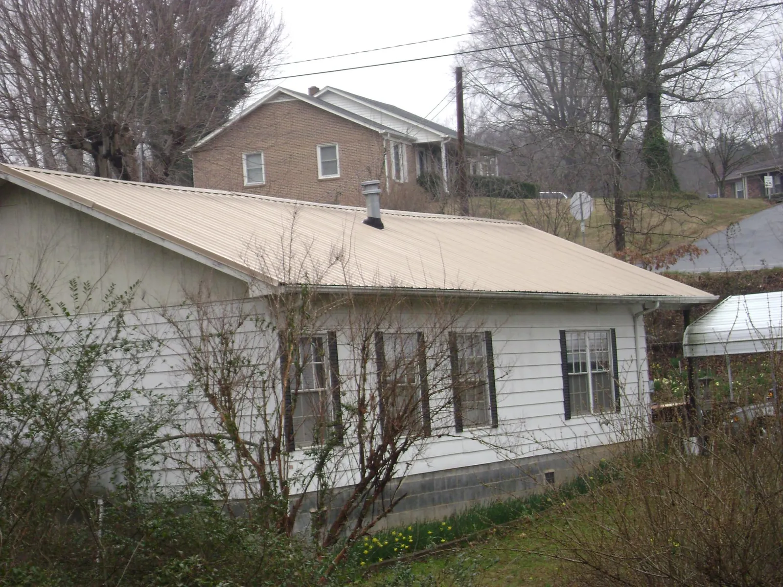 Tan metal roof on a white sided house set into a hillside — Commercial Roofing by Roofing Brothers in Los Angeles