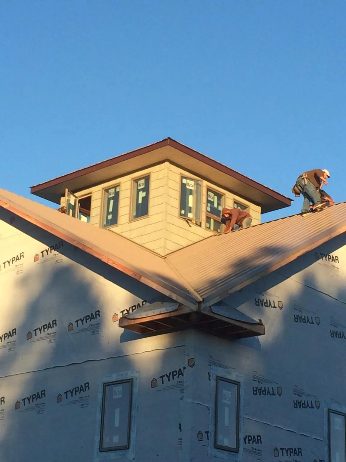 Roofers working around a rooftop cupola on a new metal roof at sunset — Roof Waterproofing in Los Angeles by Roofing Brothers